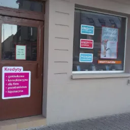 Fasada budynku z brązowymi drzwiami i oknem, na których umieszczone są naklejki i plakaty reklamujące usługi finansowe, w tym kredyty gotówkowe, konsolidacyjne, dla firm i pożyczki pozabankowe.