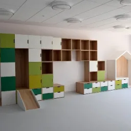 Kolorowe szafki i regały z drewna w pokoju dziecięcym, z małą zjeżdżalnią i domkiem, oświetlone światłem dziennym z okna.