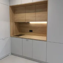 Szare szafki kuchenne z drewnianą wnęką, oświetlenie LED pod szafkami, płyta indukcyjna w blacie, minimalistyczny design.