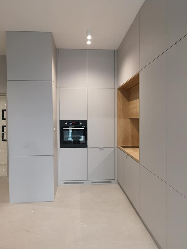 Minimalistyczna kuchnia w odcieniach szarości z zabudową na wymiar, piekarnik wkomponowany w szafkę, otwarte drewniane półki, nowoczesne oświetlenie punktowe.