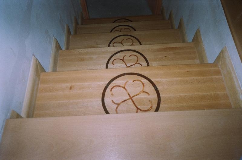 Jasne drewniane schody z ozdobnymi, okrągłymi intarsjami na stopniach, widok z dołu.