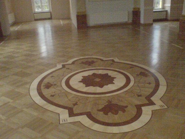 Wzór dekoracyjny z ciemnego drewna na parkiecie w przestronnym, jasnym pomieszczeniu z oknami.