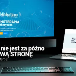 Dwa ekrany wyświetlające projekty stron internetowych: strona kliniki tlenoterapii na monitorze i strona z wyprawką dla niemowląt na laptopie, obok klawiatura i myszka.