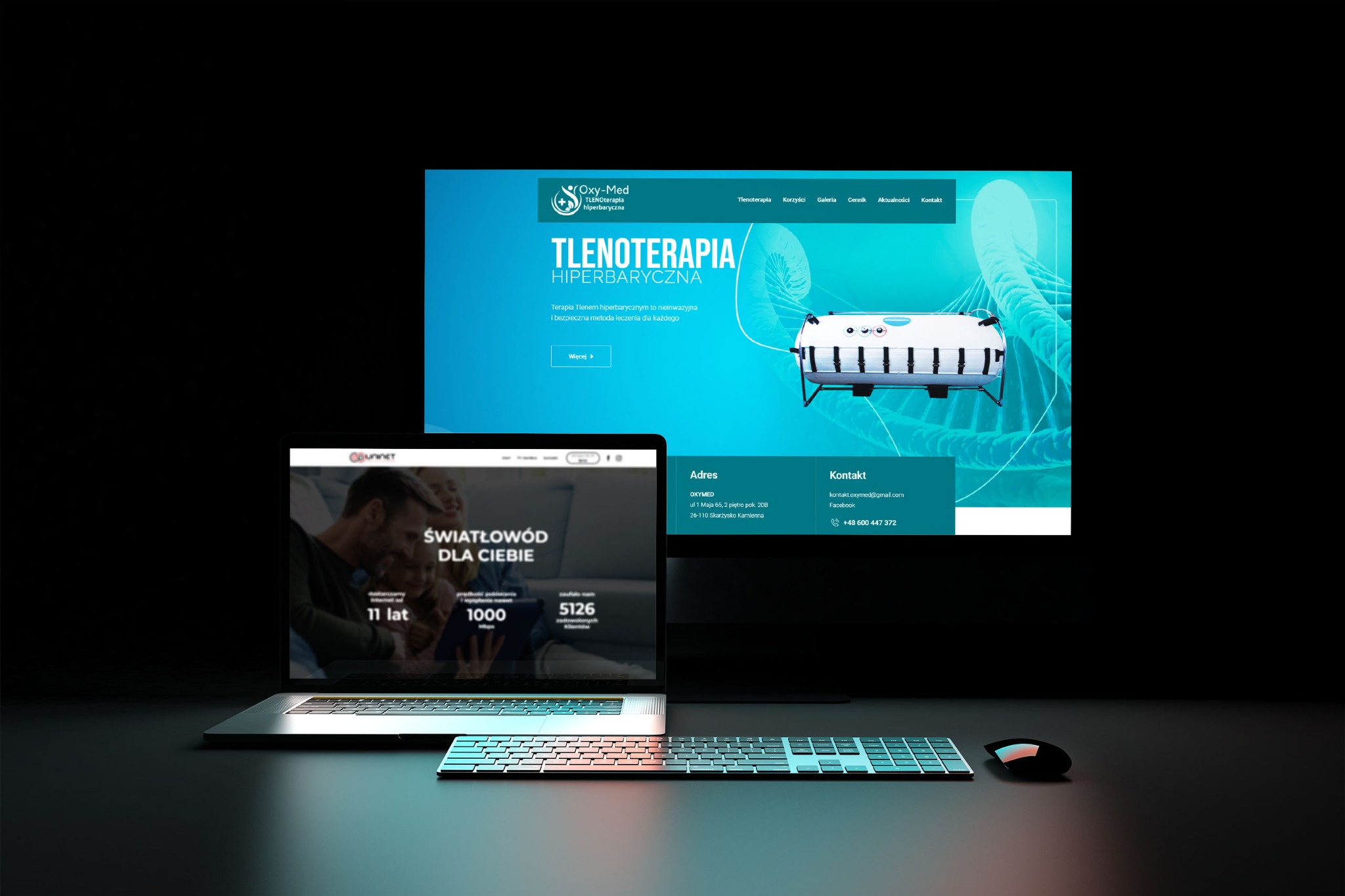 Prezentacja dwóch stron internetowych na laptopie i monitorze, z klawiaturą i myszą na biurku. Na monitorze strona o tlenoterapii hiperbarycznej, a na laptopie strona o światłowodach.