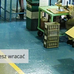 Pracownicy przy stanowiskach montażowych w hali produkcyjnej z czystą, pomalowaną podłogą z wyznaczonymi strefami.