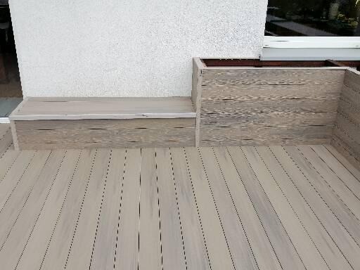 Szary taras z desek kompozytowych z zabudowaną ławką i donicą, widok z góry.