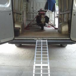 MR TRANS Małgorzata Rypień (Grupa MR Trans Przeprowadzki Warszawa) - Wnętrze busa z otwartymi drzwiami, widoczny skuter zabezpieczony pasami transportowymi i rampa najazdowa, przygotowany do transportu.