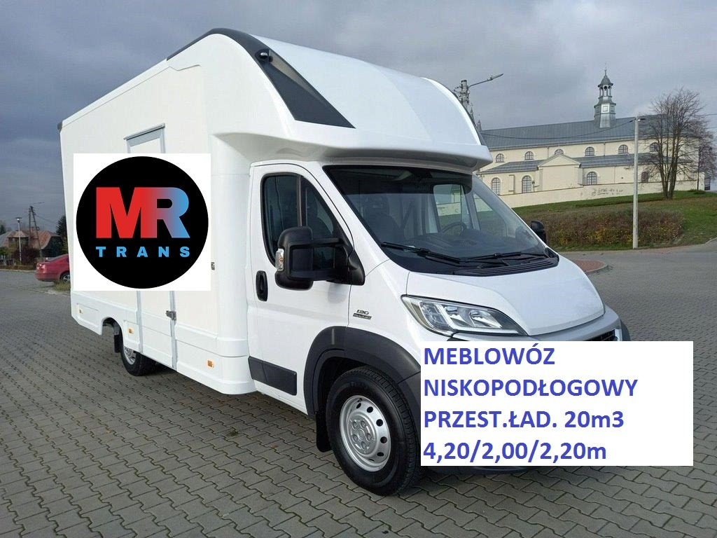 Biały bus meblowóz z logo firmy MR Trans na tle brukowanej ulicy i budynku kościelnego w oddali. Na karoserii widoczne parametry przestrzeni ładunkowej.