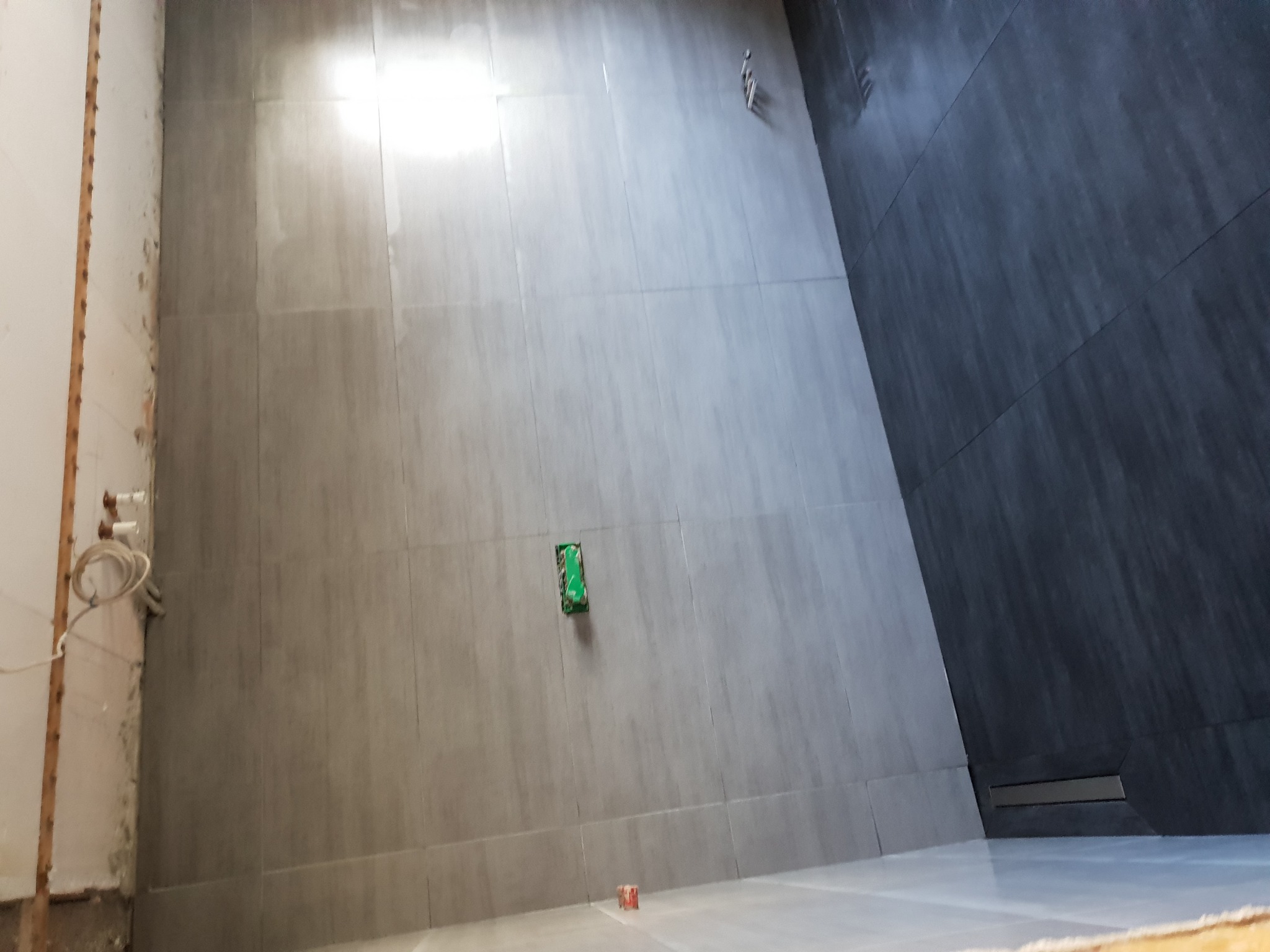 Świeżo wykafelkowana ściana w łazience z widoczną puszką elektryczną i odpływem liniowym w rogu