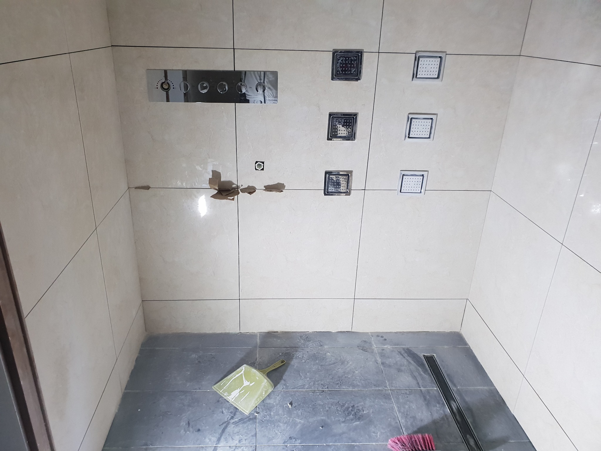 Wnętrze kabiny prysznicowej w trakcie montażu z widocznym panelem sterującym, sześcioma dyszami natryskowymi, odpływem liniowym i narzędziami do sprzątania.