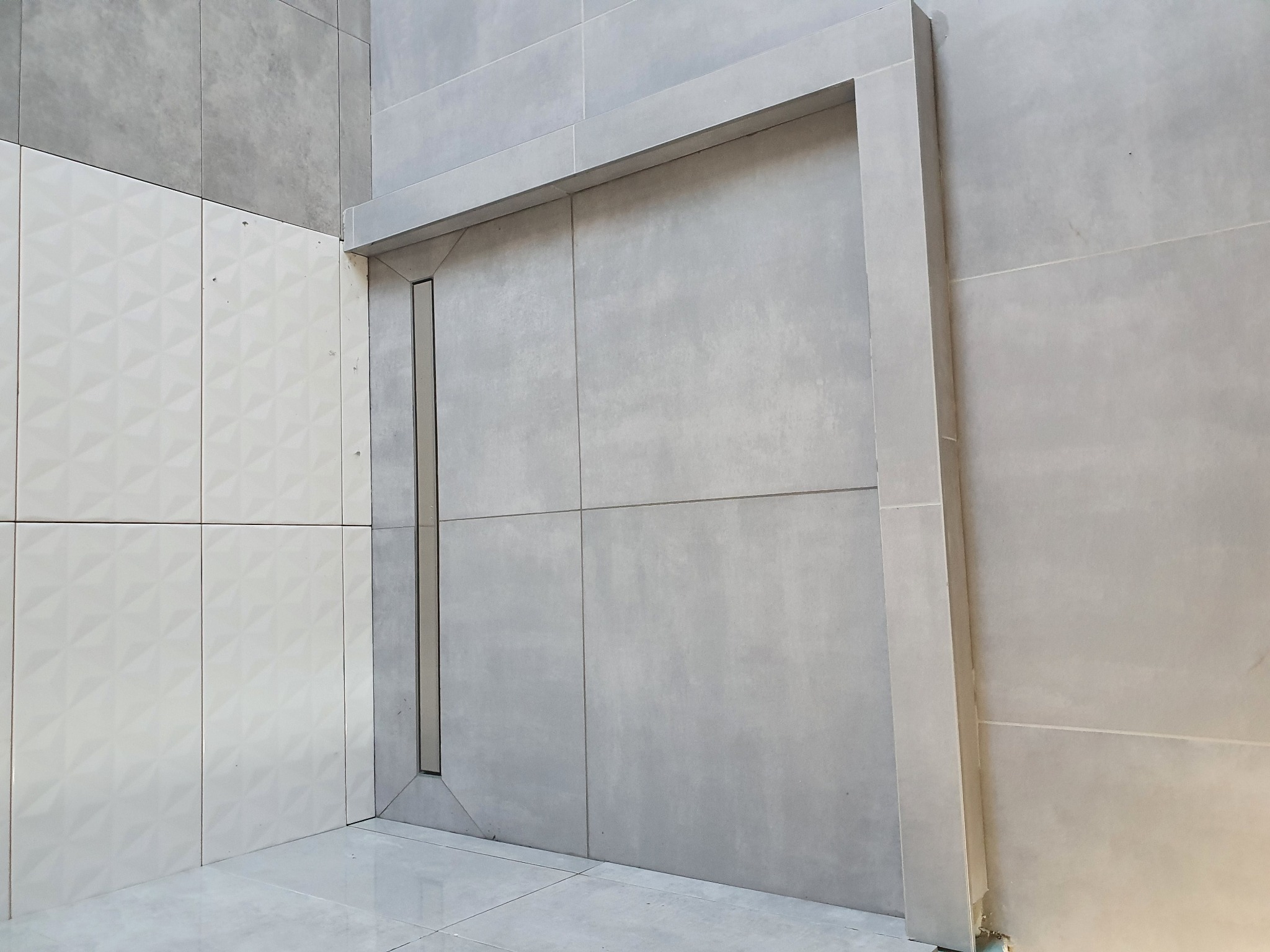 Nowoczesna łazienka z szarymi płytkami wielkoformatowymi i dekoracyjną ścianą z białych płytek z trójwymiarowym wzorem.