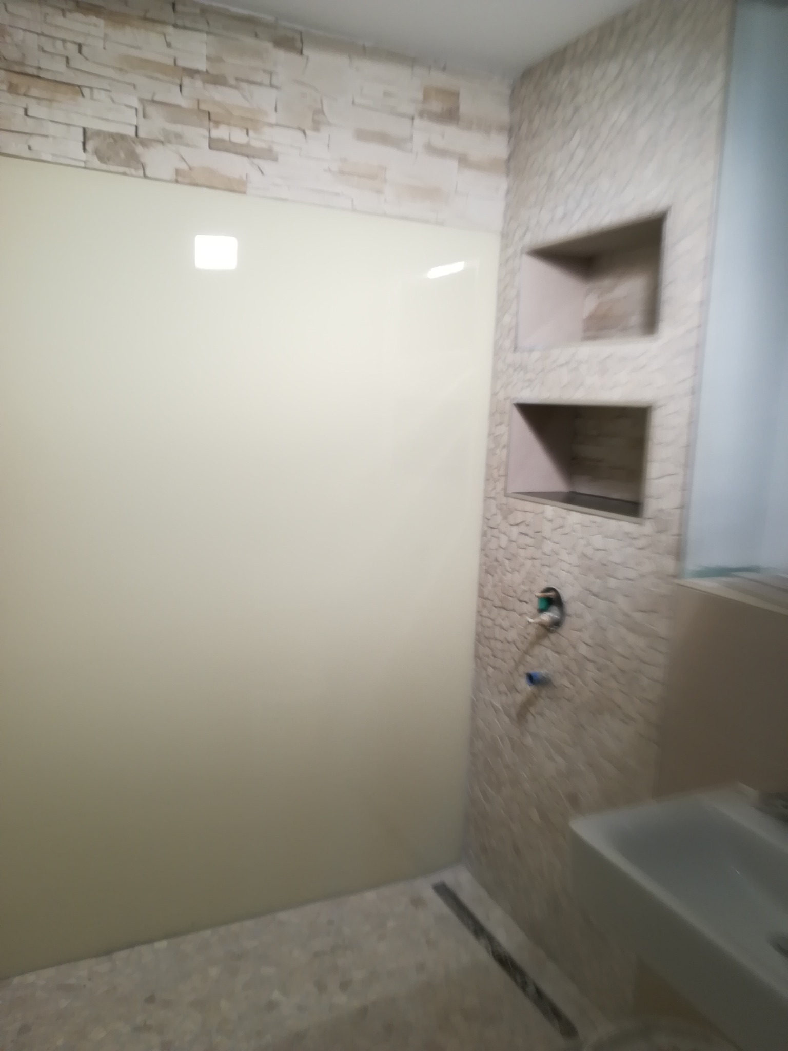 Nowoczesna łazienka z jasną, szklaną kabiną prysznicową, ścianą wyłożoną dekoracyjną mozaiką imitującą kamień i wnękami w ścianie.