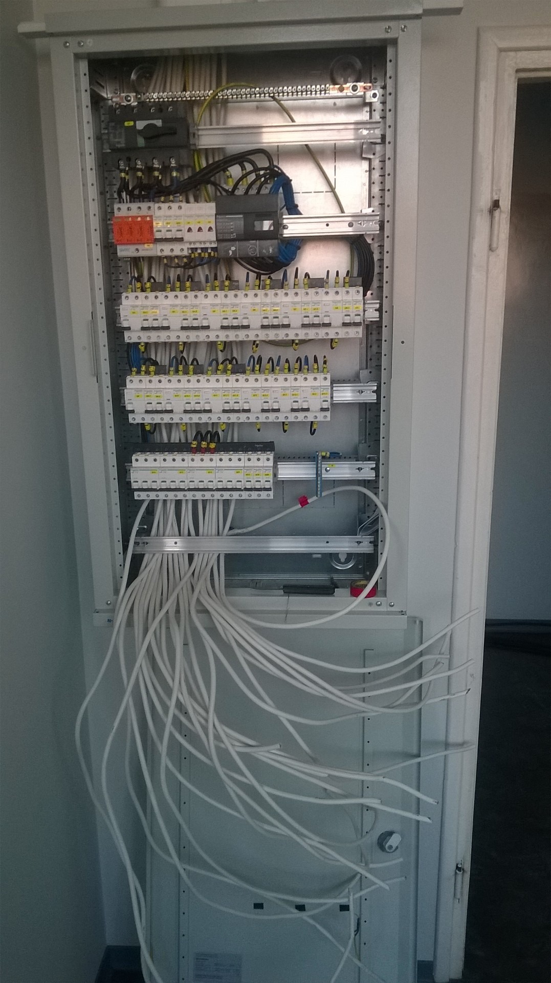 Otwarta szafa elektryczna z licznymi zabezpieczeniami i przewodami w Trzcińsku-Zdroju, widoczne białe kable wychodzące z dolnej części szafy.