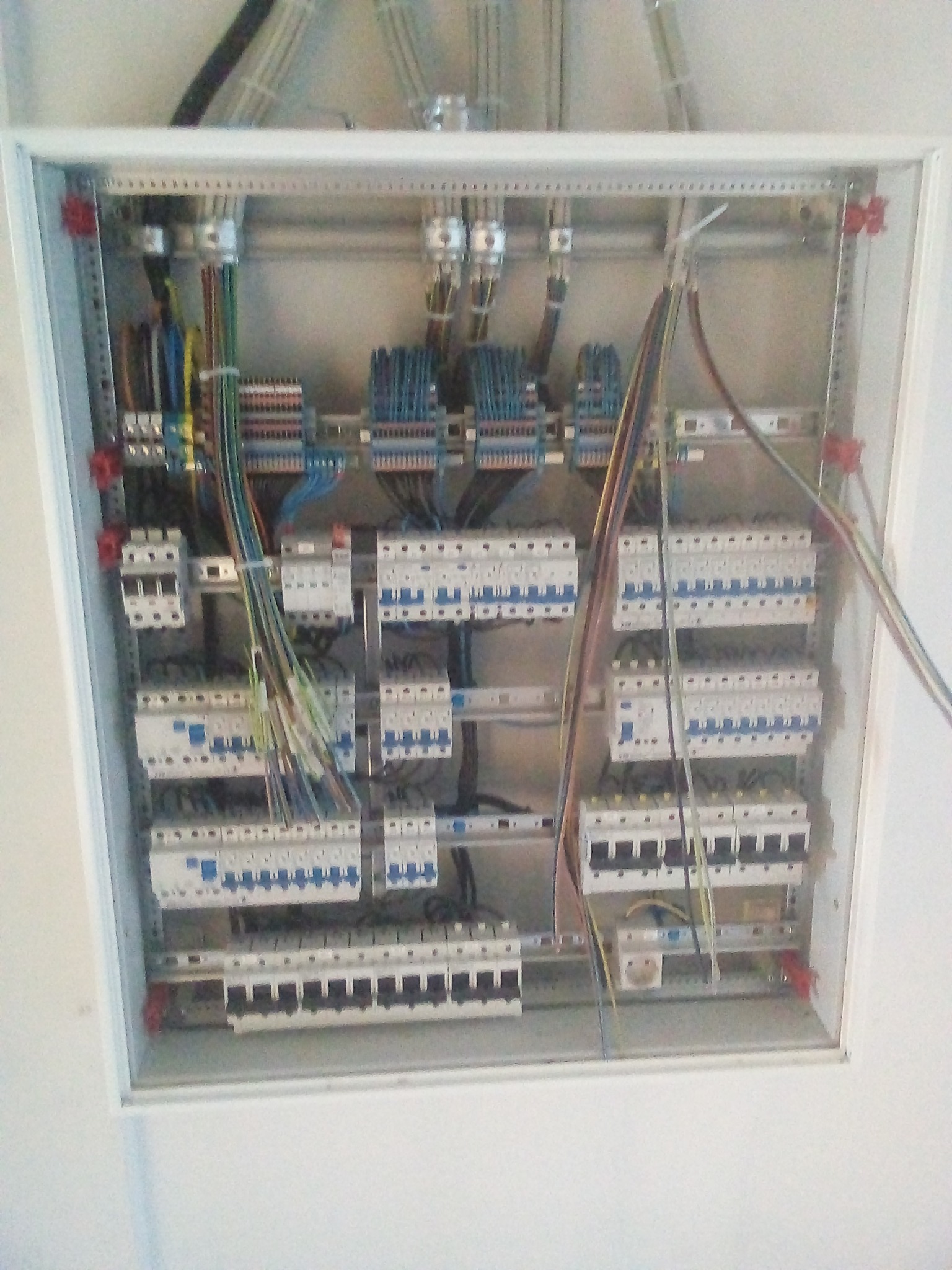 Rozdzielnica elektryczna z licznymi bezpiecznikami i przewodami, widok z góry, częściowo zamontowana w białej obudowie.