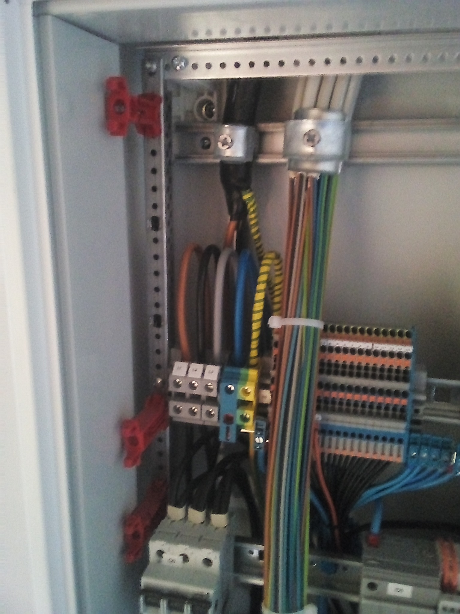 Wnętrze szafy elektrycznej z widocznymi przewodami, listwami zaciskowymi, bezpiecznikami i elementami mocującymi, uporządkowane kable w różnych kolorach.