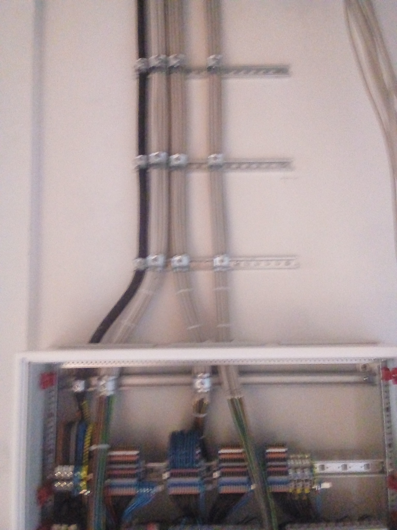 Rozdzielnia elektryczna z widocznymi kablami przymocowanymi do ściany za pomocą metalowych uchwytów.