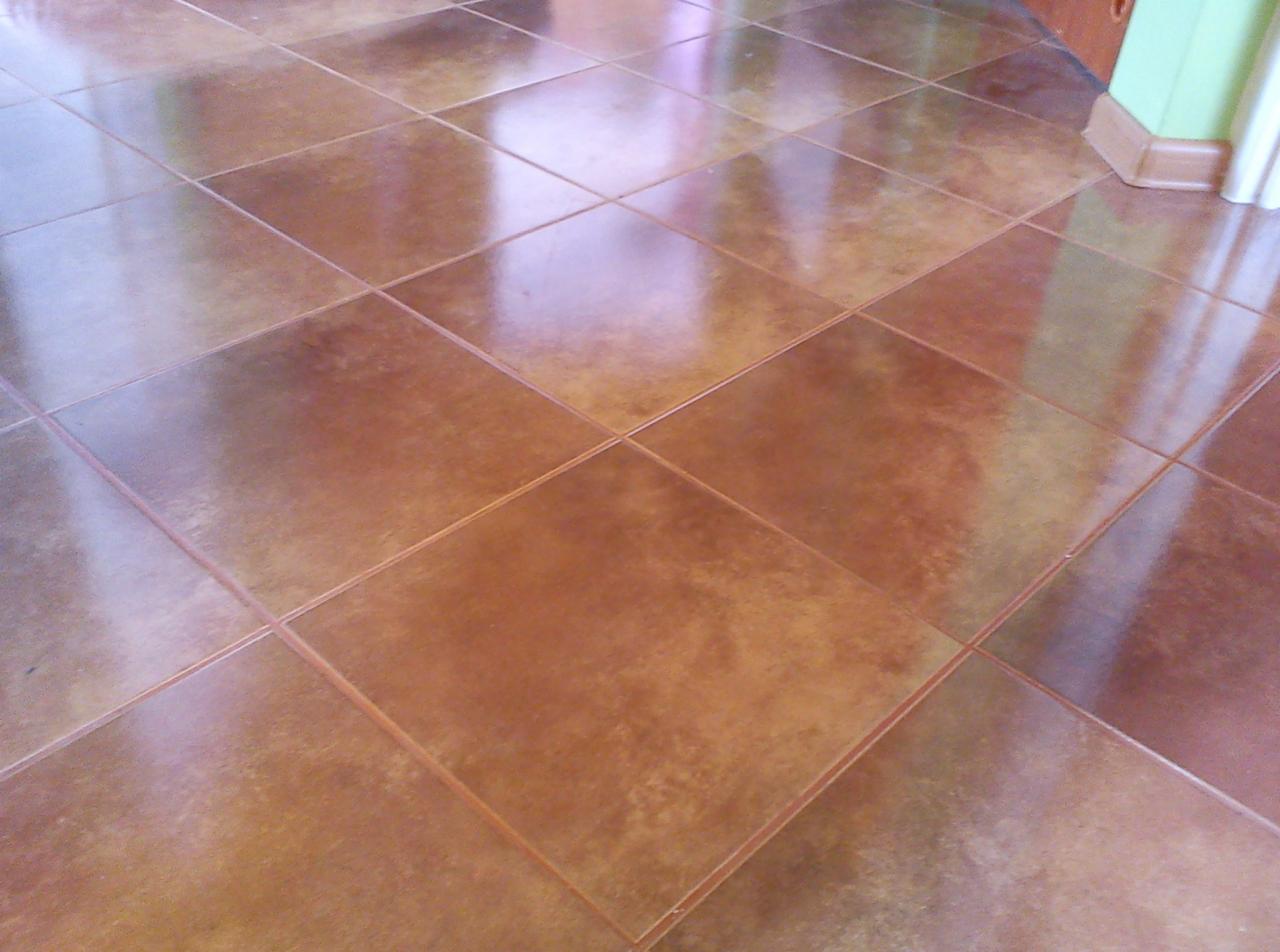 Błyszcząca, brązowa terakota ułożona kwadratowo na podłodze, widoczna listwa przypodłogowa przy ścianie.