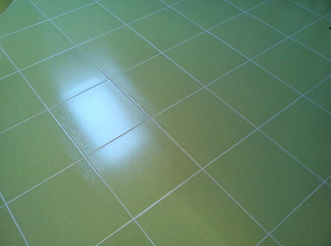 Świeżo położona, błyszcząca, jasnozielona podłoga z płytek ceramicznych, widoczne białe fugi i odbicie światła.
