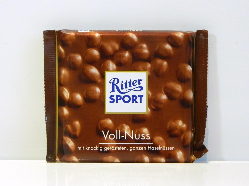 Czekolada Ritter Sport Voll-Nuss w brązowym opakowaniu z wyraźnie widocznymi całymi orzechami laskowymi na powierzchni czekolady.