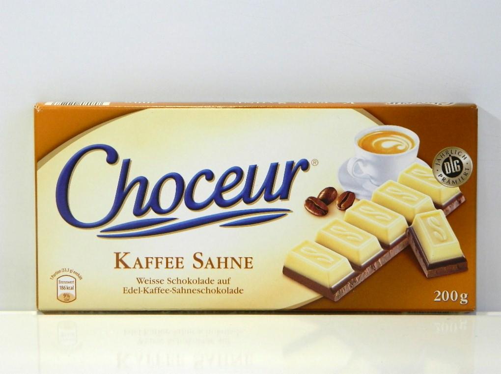 Opakowanie czekolady Choceur Kaffee Sahne z widocznymi kostkami białej czekolady z kawą, obok filiżanka kawy i ziarna kawy.