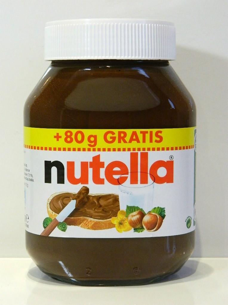 Słoik Nutelli z żółtym paskiem informującym o +80g gratis, na etykiecie rysunek kanapki z Nutellą, orzechów laskowych i szklanki mleka.