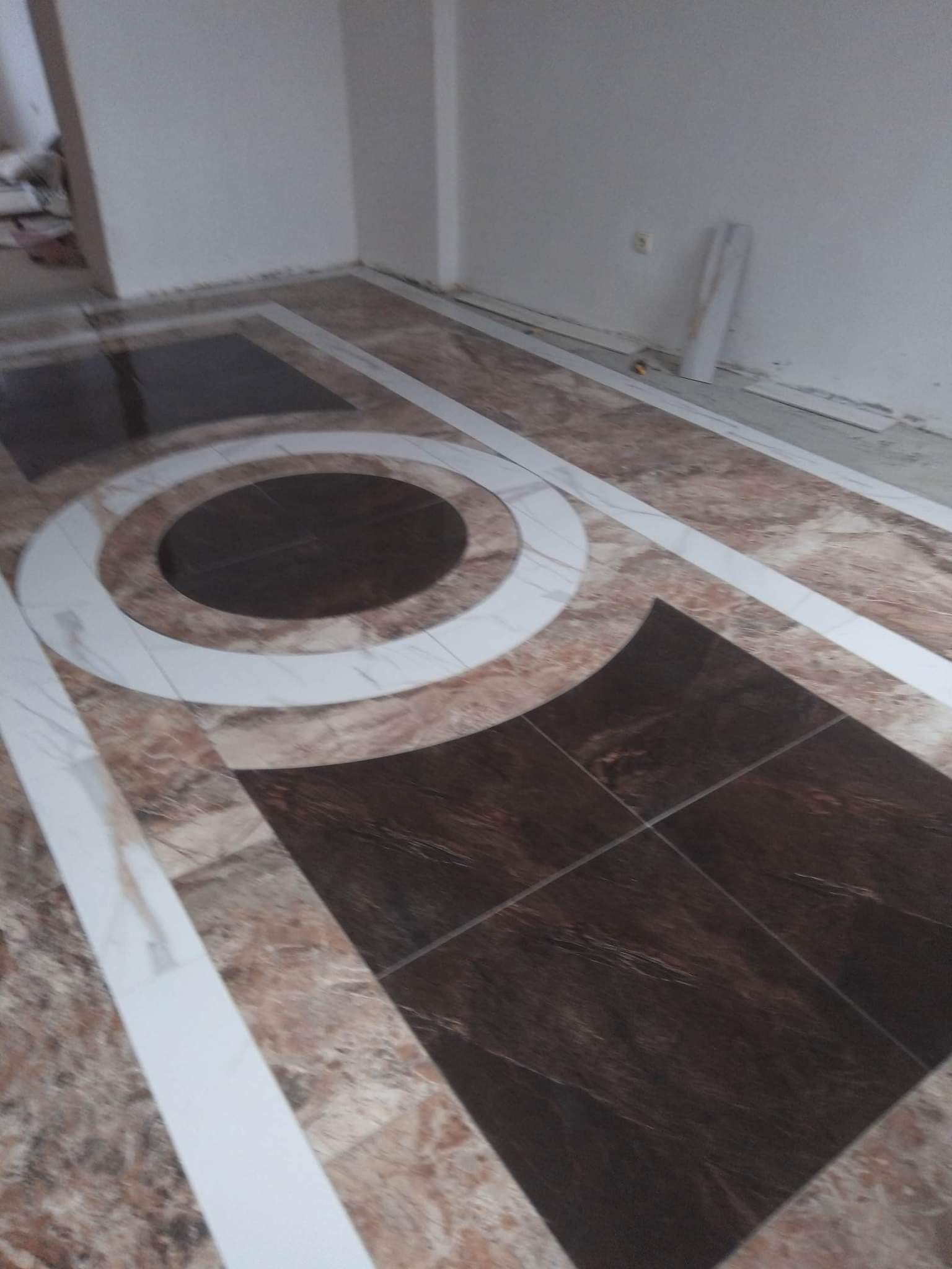 Wzorzysta podłoga z brązowych i beżowych płytek z białymi akcentami w kształcie okręgów i pasów, ułożona w pomieszczeniu w Gnieźnie, częściowo wykończona listwami przypodłogowymi.