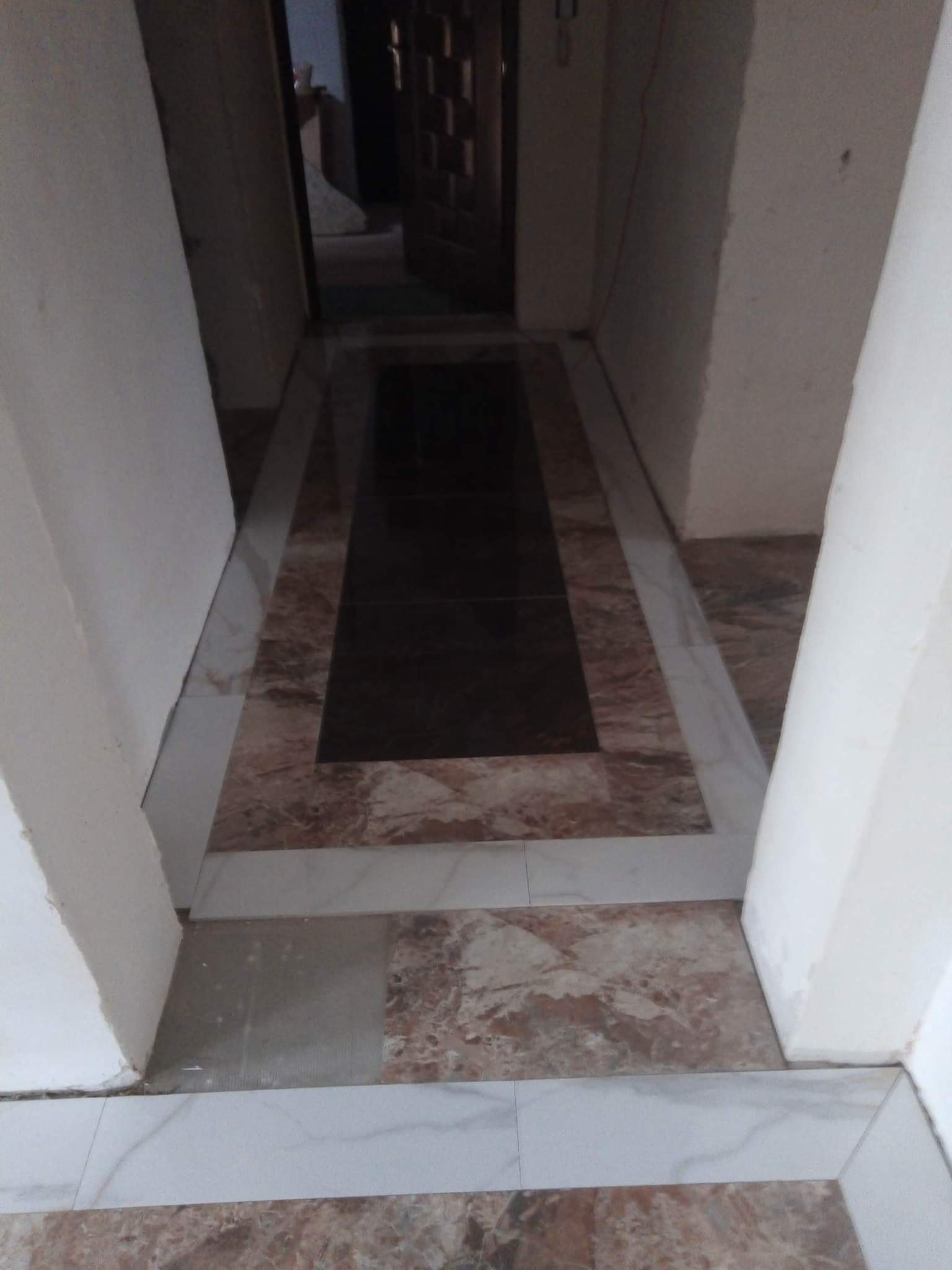 Ułożona podłoga z płytek w korytarzu, z ciemnym pasem na środku i jasnymi obramowaniami, widoczne niedociągnięcia przy łączeniu z futryną.