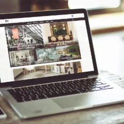 Laptop wyświetlający stronę internetową interityhome.pl z galerią zdjęć wnętrz, obok telefon i kubek na drewnianym stole.