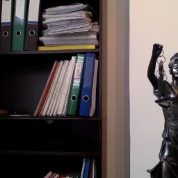 Półka z segregatorami i stosem dokumentów obok statuetki Temidy z podniesionymi wagami i mieczem