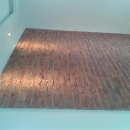 Ściana wykończona cegłą klinkierową w pomieszczeniu z białymi ścianami i wbudowanymi punktowymi lampami oświetleniowymi.