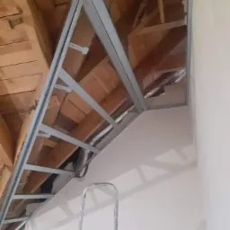 Metalowa konstrukcja szkieletowa pod płytę karton-gips na skośnym poddaszu z widoczną izolacją, drabina oparta o ścianę.