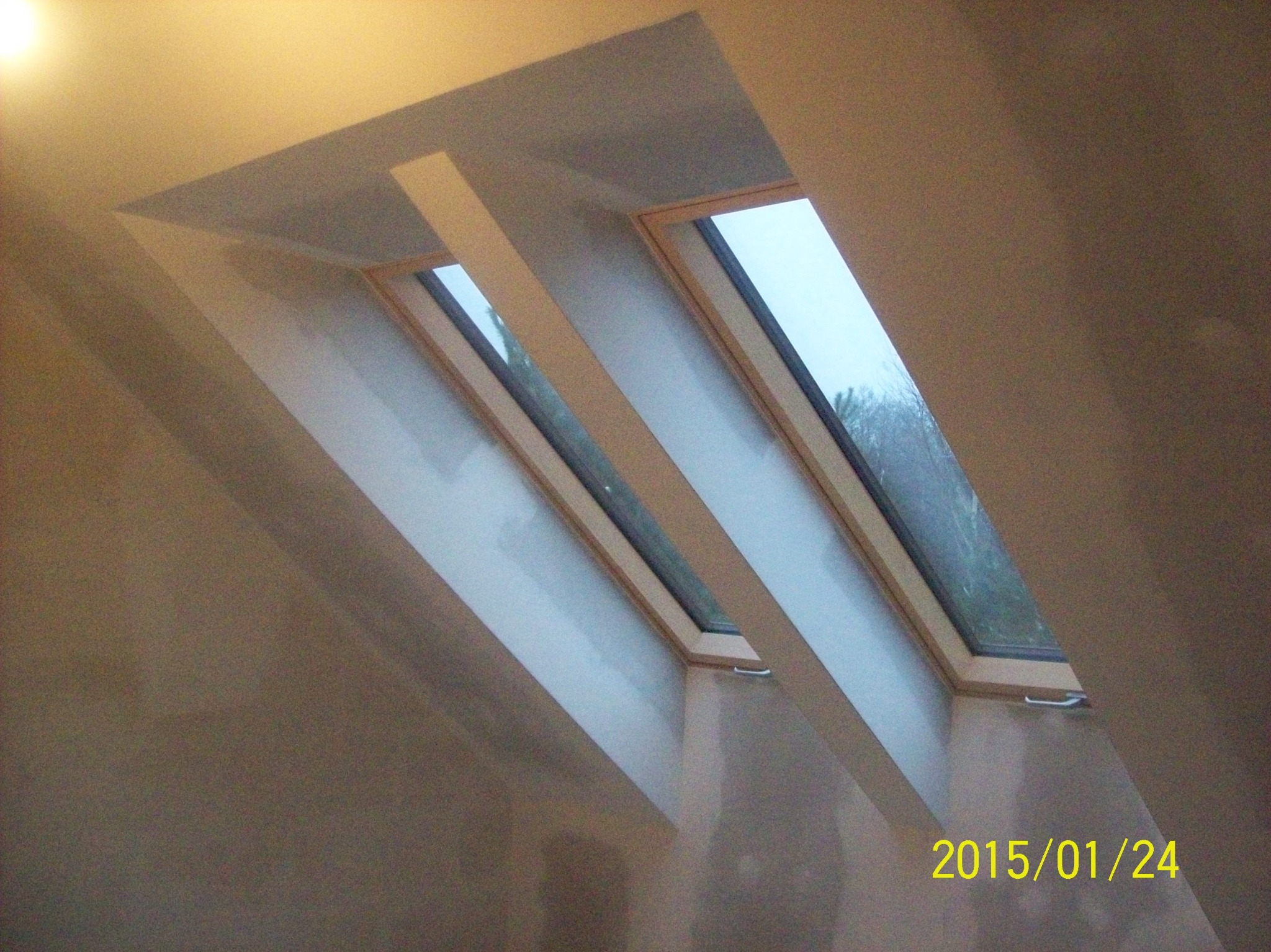 Dwa okna dachowe w skośnym suficie poddasza po nałożeniu gładzi szpachlowej, widoczne niedoskonałości i nierówności powierzchni przed szlifowaniem. Data 2015/01/24 w prawym dolnym rogu.