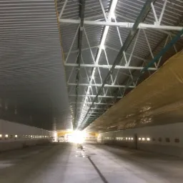 Wnętrze hali z widoczną konstrukcją stalową dachu, oświetleniem w ścianach i częściowo zamontowaną izolacją.