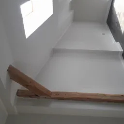 Wnętrze po remoncie: białe ściany, drewniana belka stropowa, okno dachowe i fragment ciemnej podłogi z paneli.