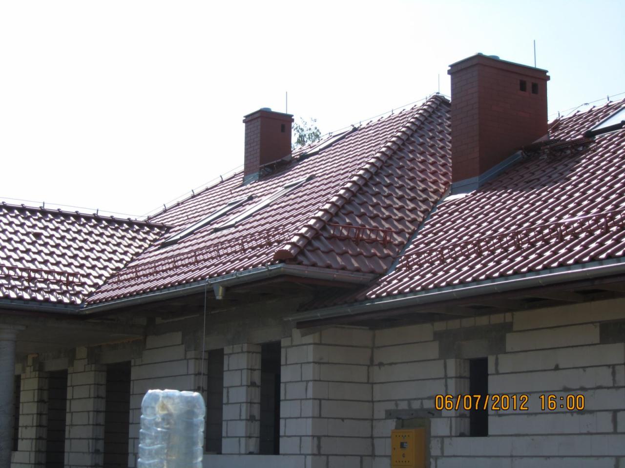 Czerwona dachówka karpiówka na dachu domu w trakcie budowy, widoczne kominy i system rynnowy, instalacja odgromowa.