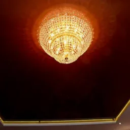 Błyszczący, kryształowy żyrandol pod ciemnobrązowym, lustrzanym sufitem napinanym z subtelnym oświetleniem LED na obrzeżach.