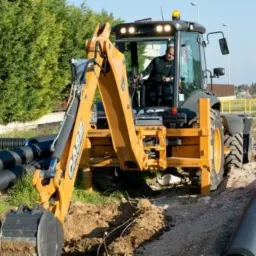 Żółta maszyna budowlana CASE z operatorem kopie rów obok ułożonych rur kanalizacyjnych na placu budowy.