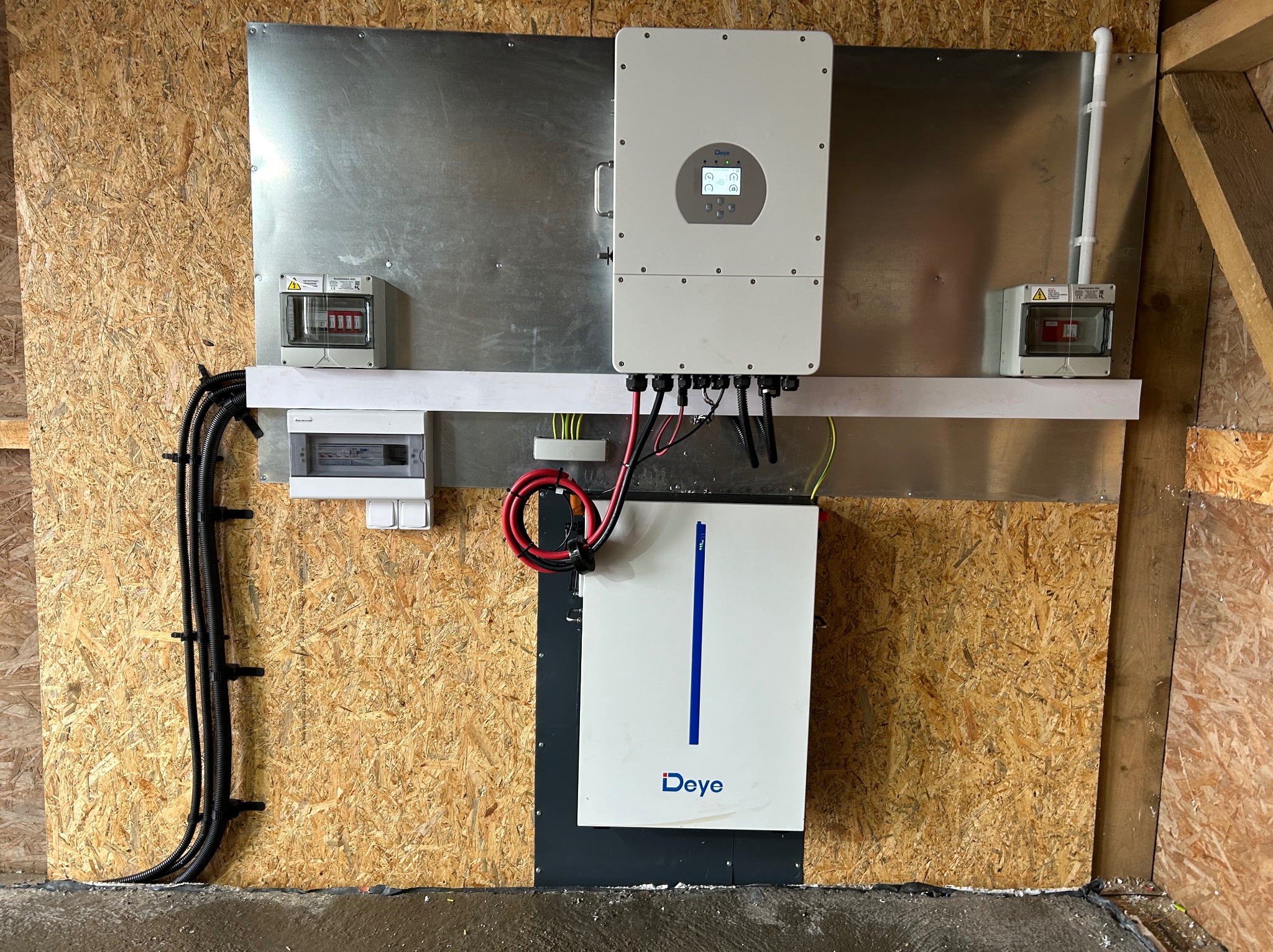 Kompletna instalacja fotowoltaiczna wewnątrz budynku: inwerter Deye, magazyn energii, zabezpieczenia elektryczne i okablowanie na płycie OSB. Widok z bliska.