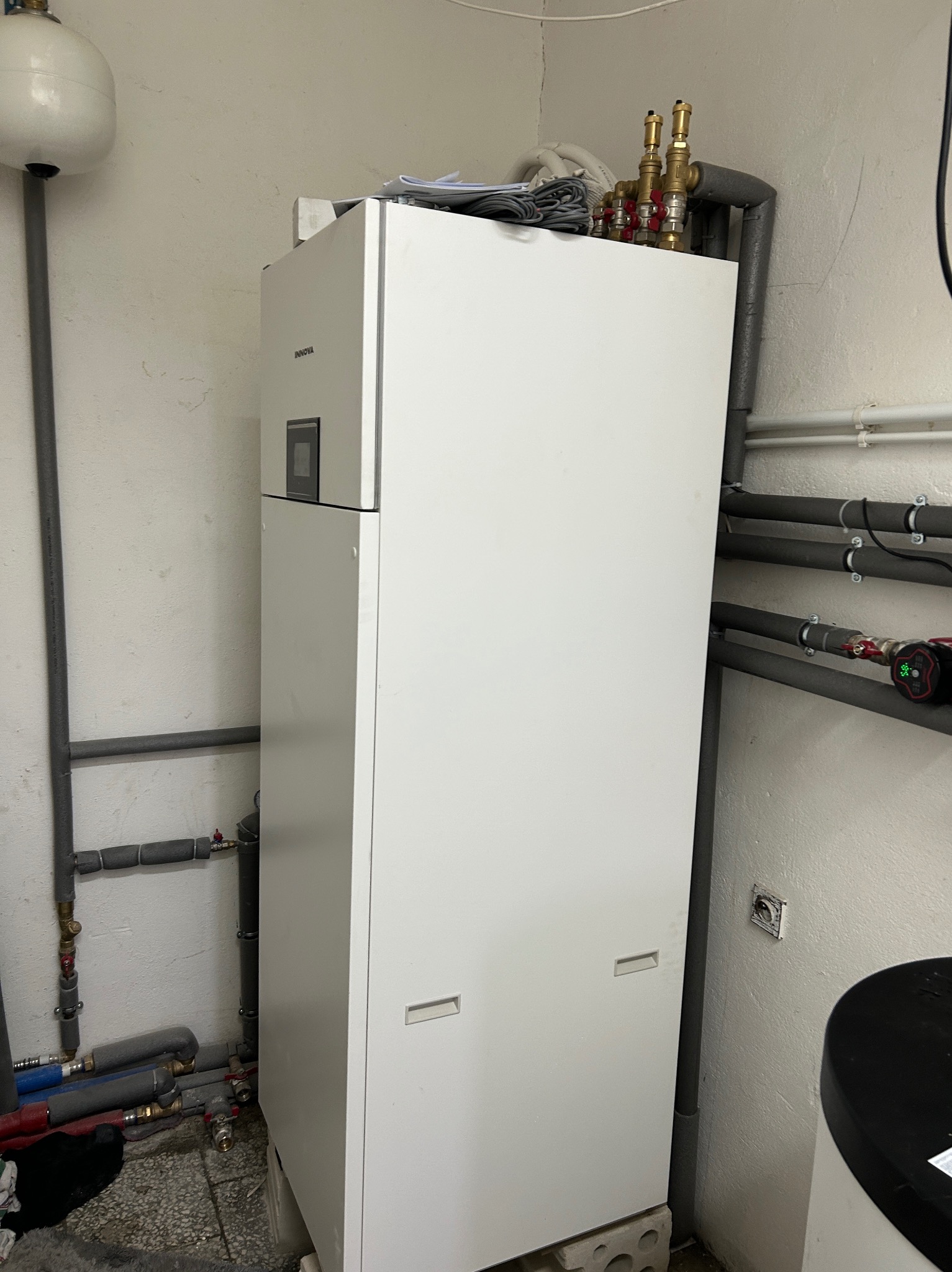 Biały, nowoczesny piec grzewczy Innova w kotłowni, z widocznymi rurami instalacji CO i elementami armatury. Ujęcie z bliska, podkreślające detale instalacji.