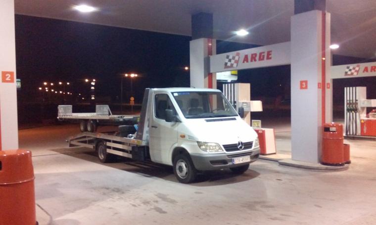 Biała laweta Mercedes na stacji benzynowej ARGE nocą. Przyczepa do transportu pojazdów. Widoczne dystrybutory i oświetlenie stacji.