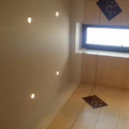 Jasna łazienka z beżowymi płytkami, oświetleniem punktowym w suficie i dekoracyjnym pasem płytek z motywem roślinnym przy oknie.