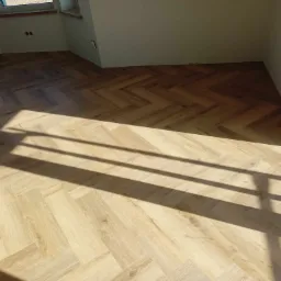 Jasne panele ułożone w jodełkę w nowym wnętrzu, oświetlone promieniami słońca. Realizacja z Brzeska. Widoczne gniazdka elektryczne.