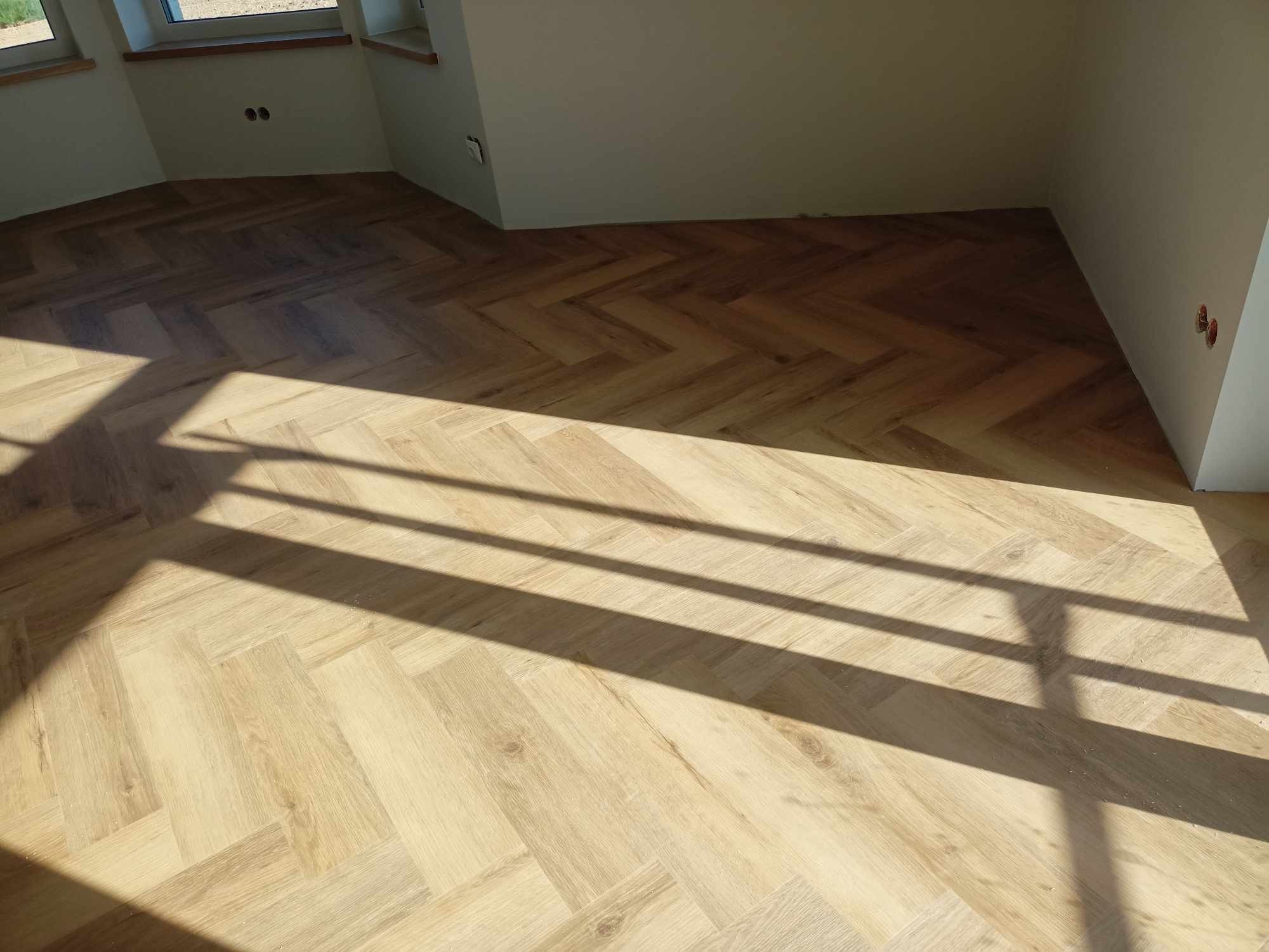 Jasne panele ułożone w jodełkę w nowym wnętrzu, oświetlone promieniami słońca. Realizacja z Brzeska. Widoczne gniazdka elektryczne.