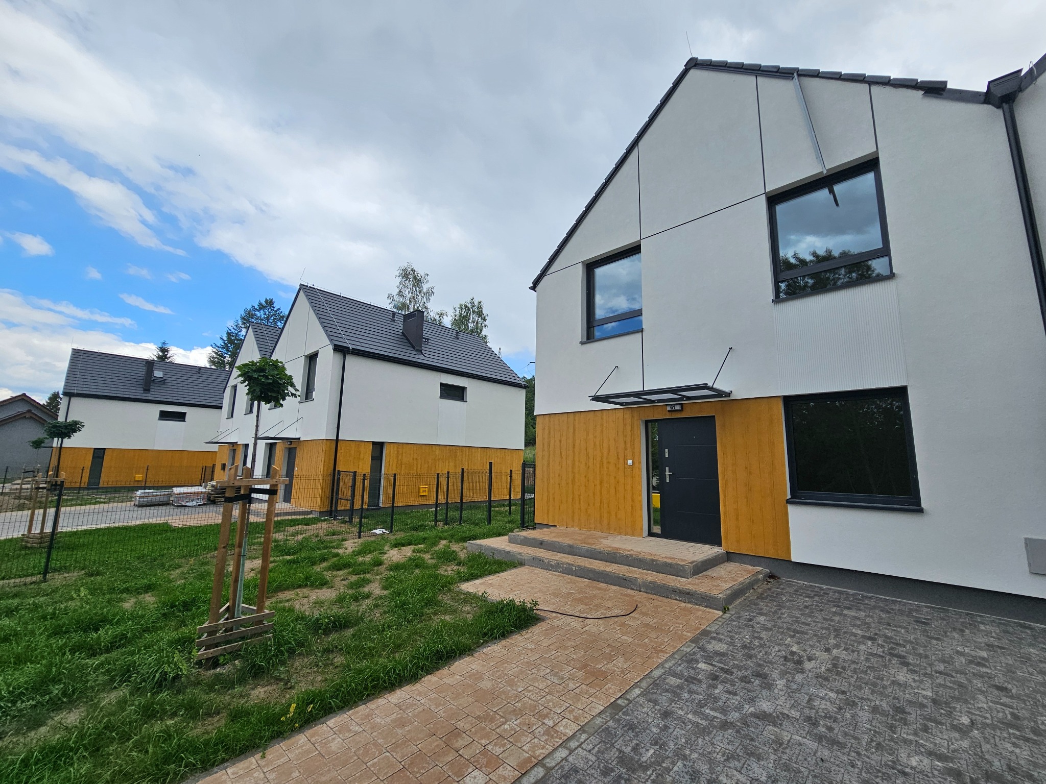 Nowoczesne domy szeregowe z białymi ścianami i drewnianą elewacją w Jeleniej Górze, widoczne z zewnątrz, z szarymi dachami i brukowanymi ścieżkami.