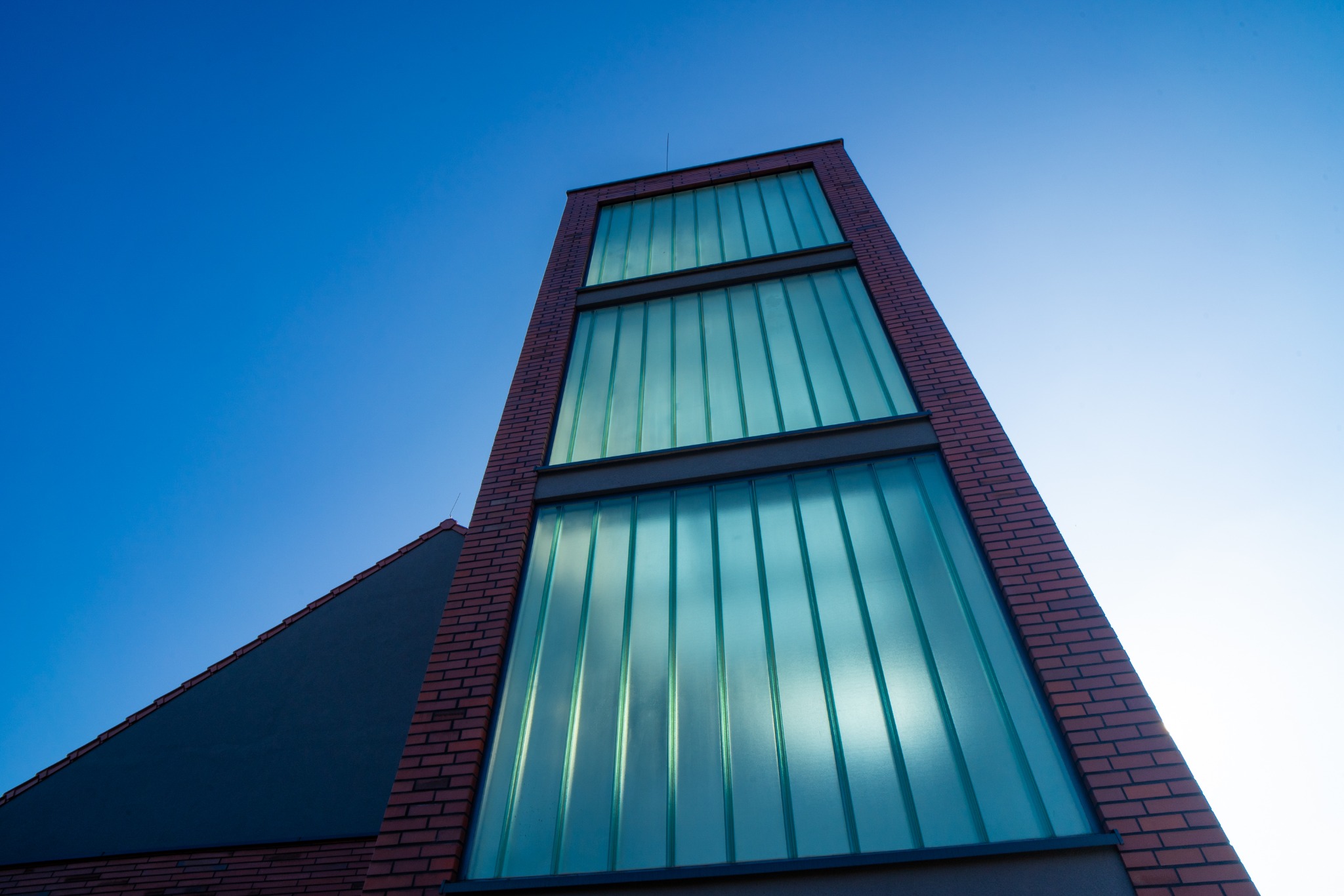 Remiza OSP w Węgrach: Nowoczesna bryła budynku z czerwonej cegły i przeszkleniami, widziana z dołu na tle błękitnego nieba.