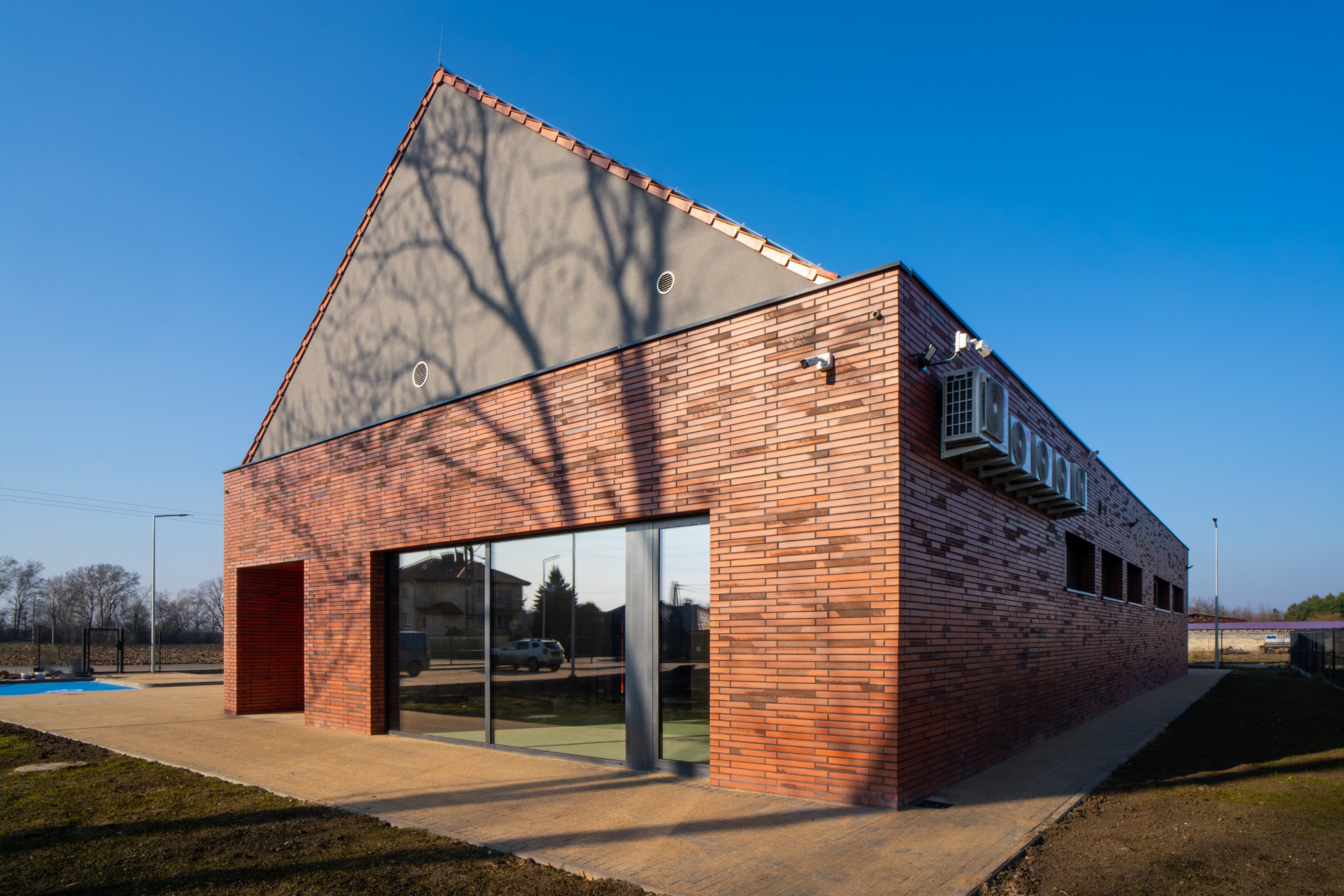 Nowoczesna remiza OSP w Węgrach koło Wrocławia. Budynek z czerwonej cegły klinkierowej, z dużymi oknami i klimatyzacją na elewacji. Widok z zewnątrz w słoneczny dzień.