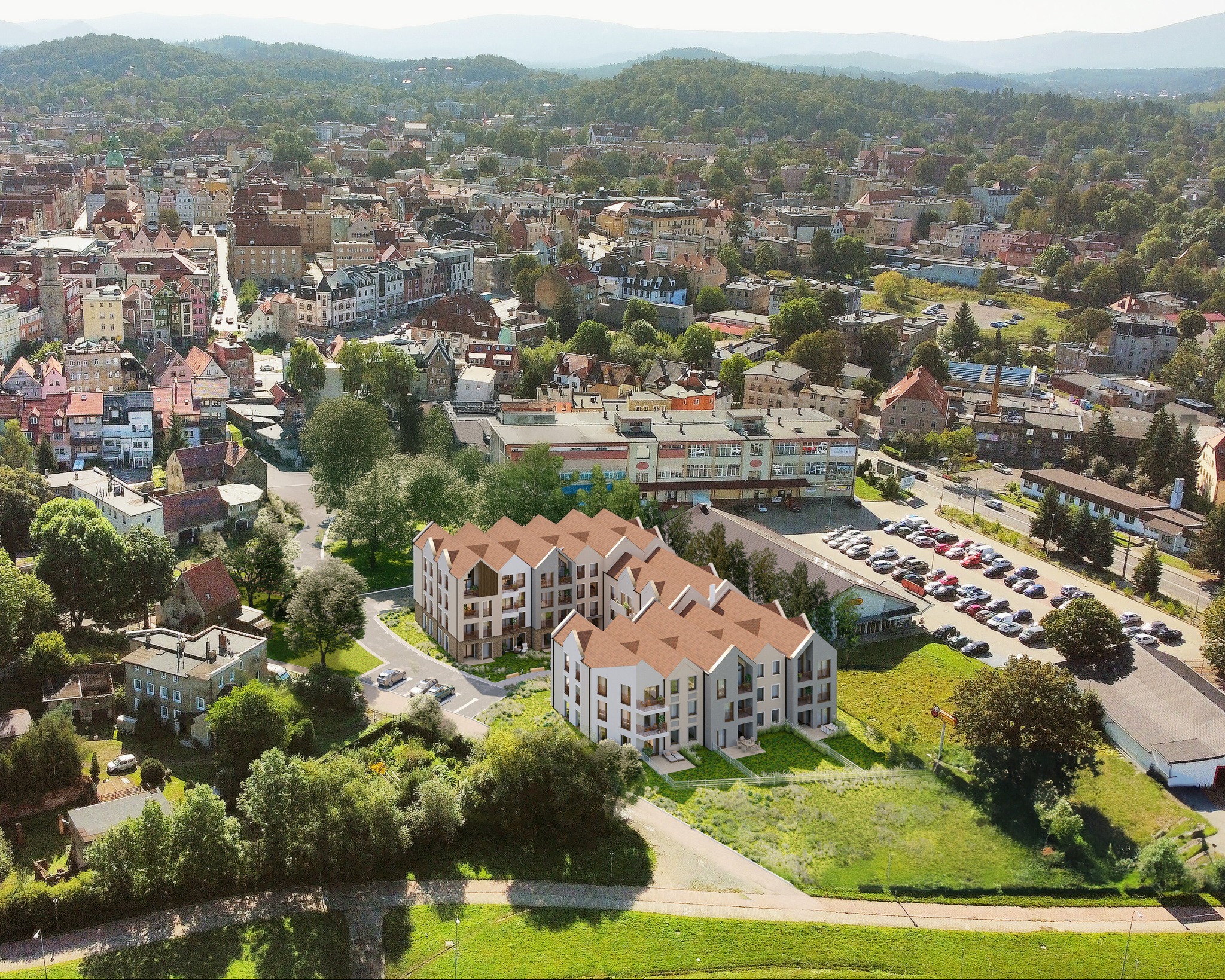 Wizualizacja osiedla Sudetia w Jeleniej Górze z lotu ptaka, ukazująca budynki z brązowymi dachami wkomponowane w krajobraz miejski. Tło stanowią góry i zabudowa miasta.