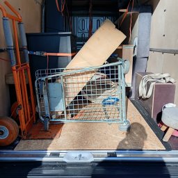 TAXI BAGAŻOWE KRAKÓW 24h7 - Wnętrze busa załadowane meblami i sprzętem do przeprowadzki, zabezpieczone pasami transportowymi. W tle widoczne drzwi pojazdu.