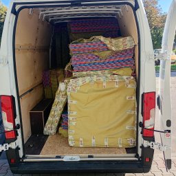 TAXI BAGAŻOWE KRAKÓW 24h7 - Wnętrze białego busa z otwartymi drzwiami, wypełnione po brzegi zapakowanymi kartonami i matami, gotowe do transportu. Widok z tyłu pojazdu.