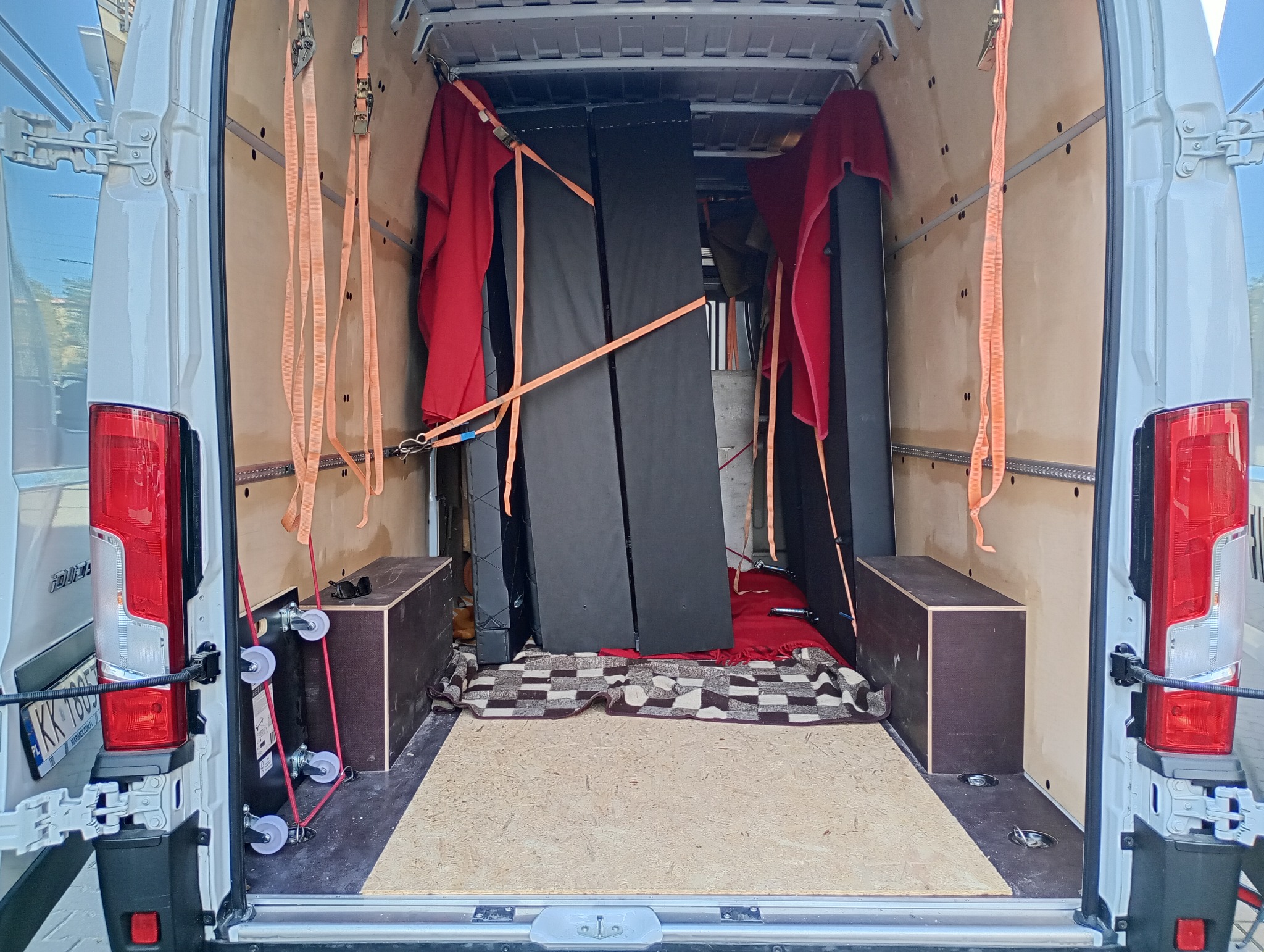 Wnętrze białego busa z zabezpieczonymi meblami i kocami, gotowego do transportu. Widoczne pasy mocujące i drewniana podłoga.
